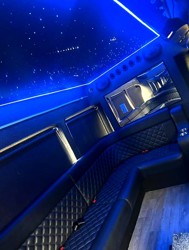 Wide-angle interior of the Ryels party bus showing quilted leather seating, ambient lighting and the entertainment screen